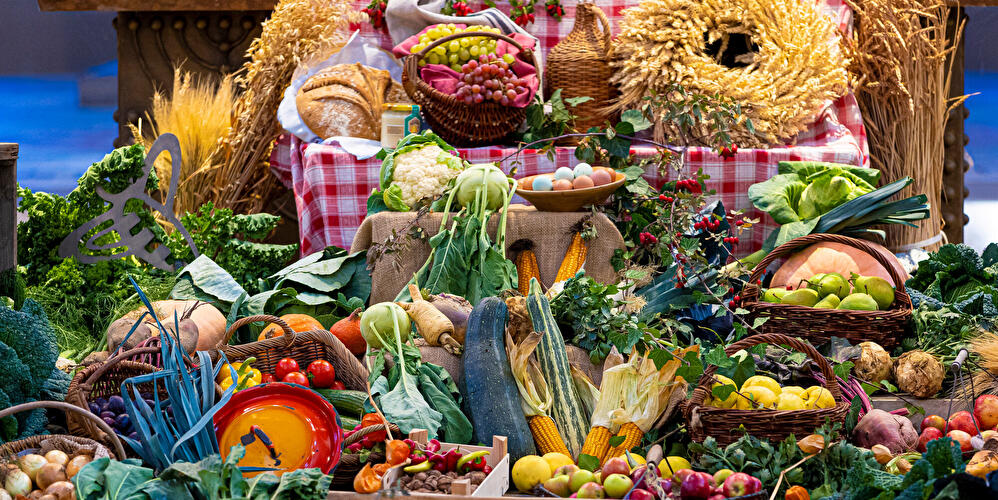 Reich gedeckter Erntedanktisch mit Obst, Gemüse, Brot, Getreidegarben und Körben voller Erntegaben als Festdekoration.