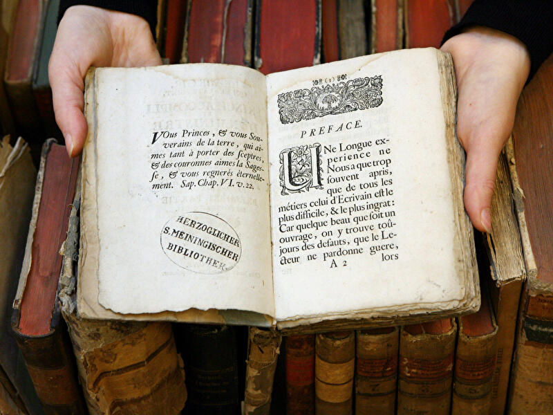 Eine Person hält ein aufgeschlagenes, stark gealtertes Buch 