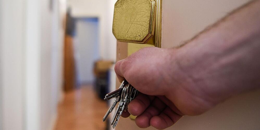 Hand öffnet Wohnungstür mit Schlüsselbund im Türschloss.