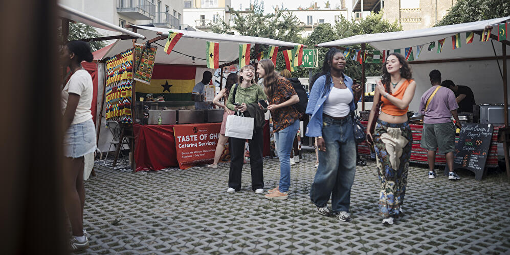 Besucher:innen zwischen Food-Ständen und Länderflaggen auf dem African Food Festival im Innenhof der Factory Berlin.