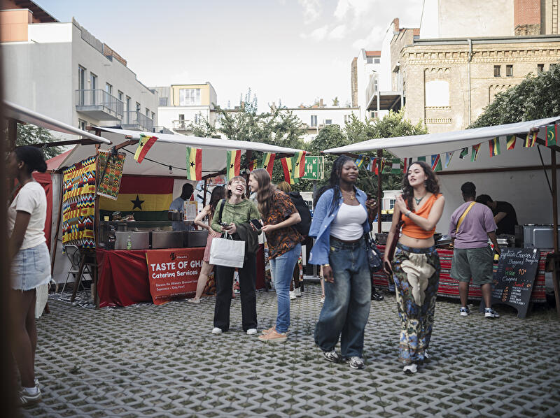 Besucher:innen zwischen Food-Ständen und Länderflaggen auf dem African Food Festival im Innenhof der Factory Berlin.