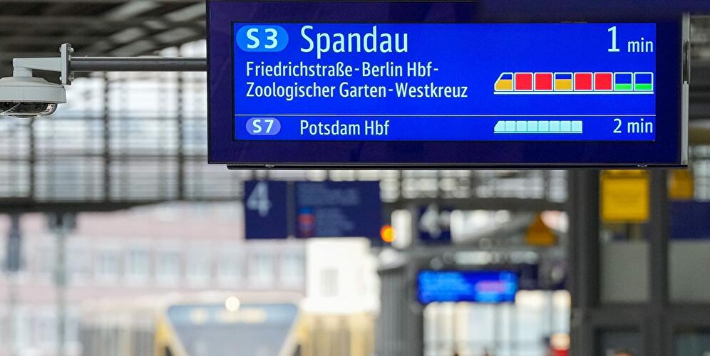 Fahrgäste unter einer Anzeigetafel für die S-Bahn nach Spandau und Potsdam.
