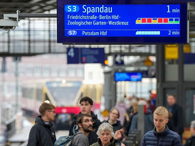 Fahrgäste unter einer Anzeigetafel für die S-Bahn nach Spandau und Potsdam.