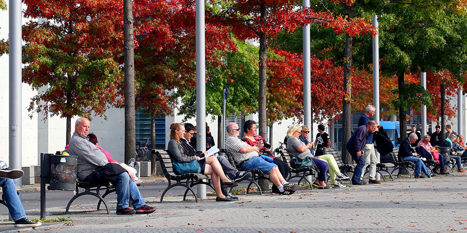 Menschen sitzen auf Parkbänken im Regierungsviertel in Berlin und genießen die warmen Strahlen der Herbstsonne.