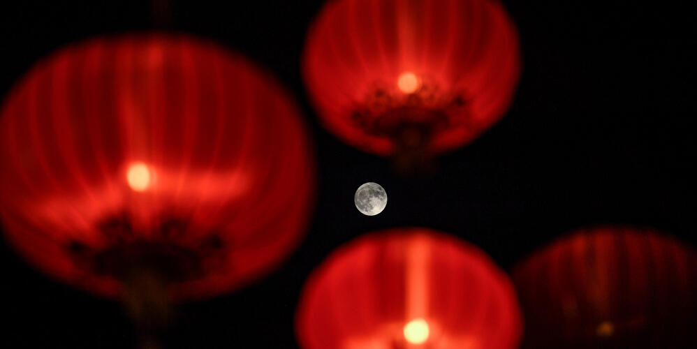 Roter Vollmond zwischen unscharf leuchtenden roten Papierlaternen vor dunklem Nachthimmel.