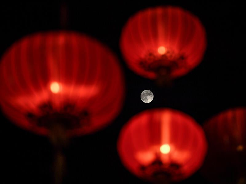 Roter Vollmond zwischen unscharf leuchtenden roten Papierlaternen vor dunklem Nachthimmel.