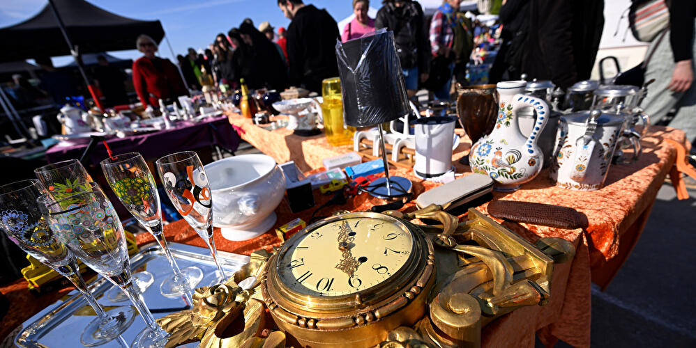 Eine alte Uhr, Sektgläser, Vasen und Tassen werden auf einem Flohmarkt angeboten.