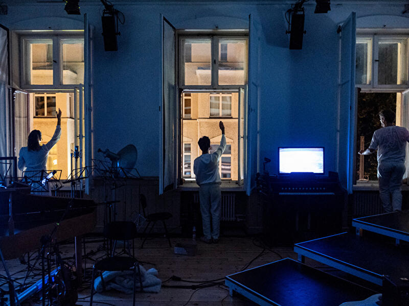 Inszenierung im Berliner Schlossplatztheater mit drei Personen vor offenen Fenstern und blauer Lichtstimmung.
