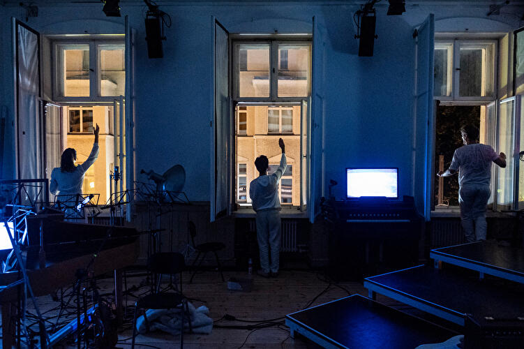 Inszenierung im Berliner Schlossplatztheater mit drei Personen vor offenen Fenstern und blauer Lichtstimmung.