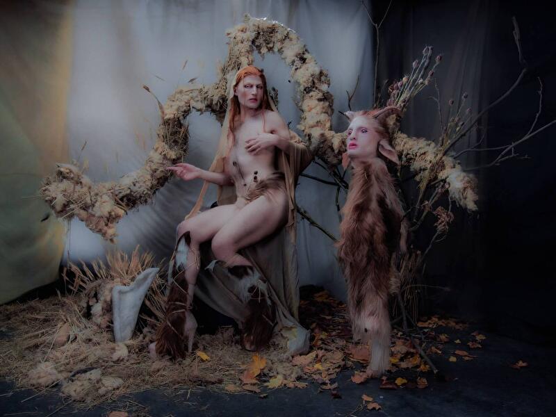 Inszenierte Fantasiefigur in naturverbundener Kulisse mit Fell, Zweigen und Blüten, Teil einer künstlerischen Performance.