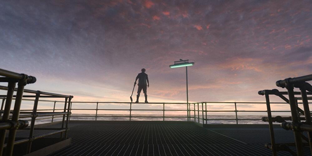 Silhouette einer Person mit Spaten auf einer Plattform vor Meer und farbigem Abendhimmel.