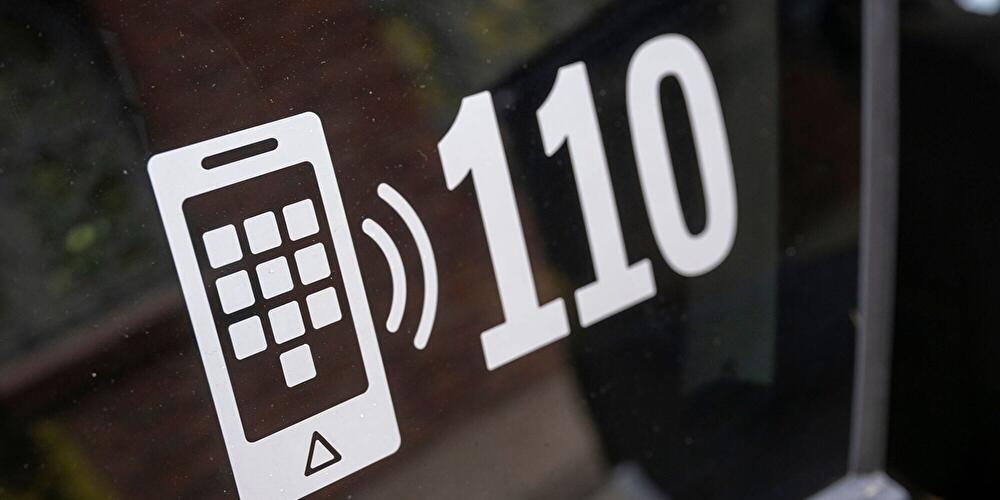 Piktogramm für Notruf 110 mit Smartphone-Symbol auf einer Glasscheibe.