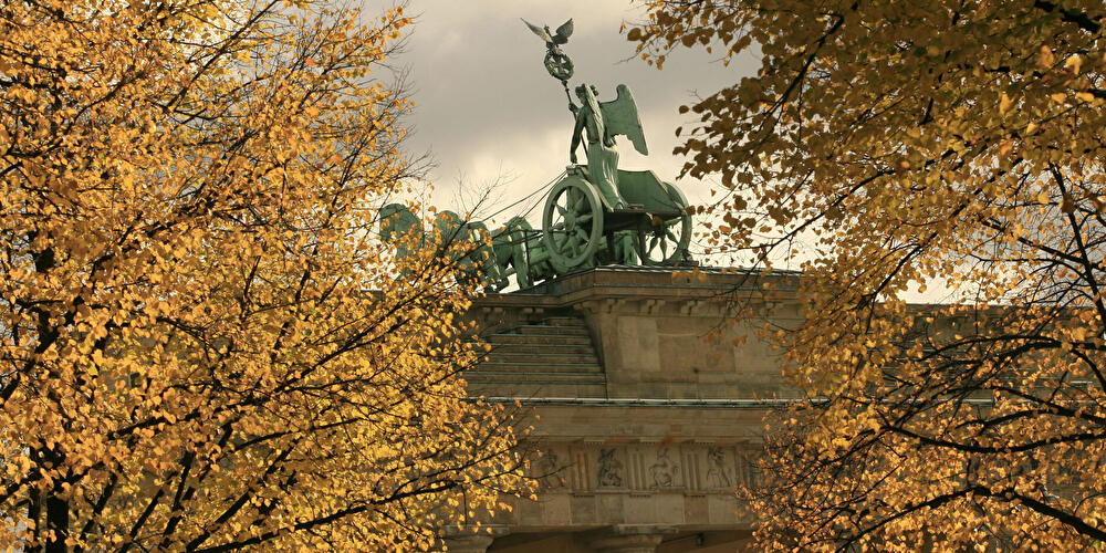 Quadriga auf dem Brandenburger Tor, eingerahmt von goldgelben Herbstbäumen unter bewölktem Himmel in Berlin.