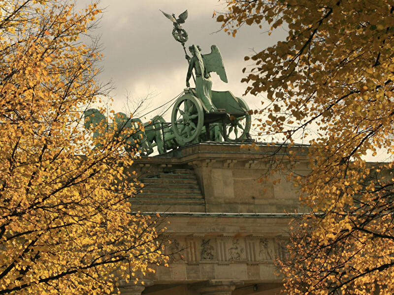 Quadriga auf dem Brandenburger Tor, eingerahmt von goldgelben Herbstbäumen unter bewölktem Himmel in Berlin.