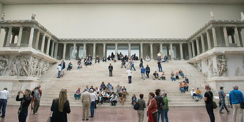Besucherinnen und Besucher auf der breiten Freitreppe der Antikensammlung im lichtdurchfluteten Pergamonmuseum.