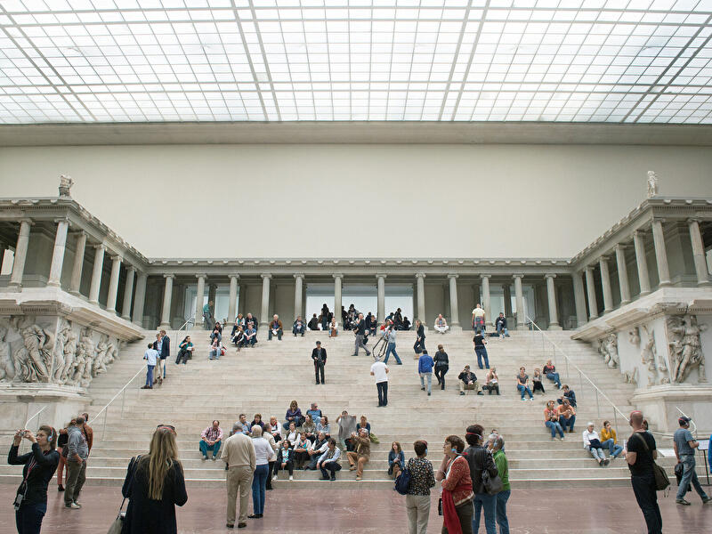 Besucherinnen und Besucher auf der breiten Freitreppe der Antikensammlung im lichtdurchfluteten Pergamonmuseum.