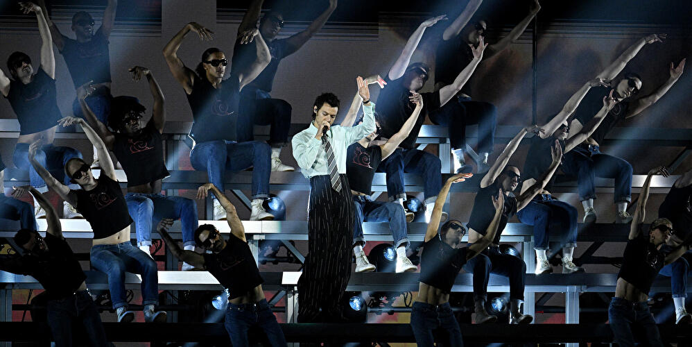 Harry Styles bei einer aufwendigen Bühnenshow mit Tänzerensemble und Spotlights.