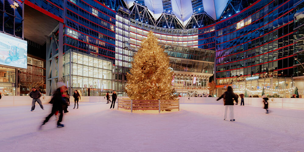 Eisbahn mit beleuchtetem Weihnachtsbaum in der Mitte und Menschen beim Schlittschuhlaufen vor dem Sony Center am Potsdamer Platz