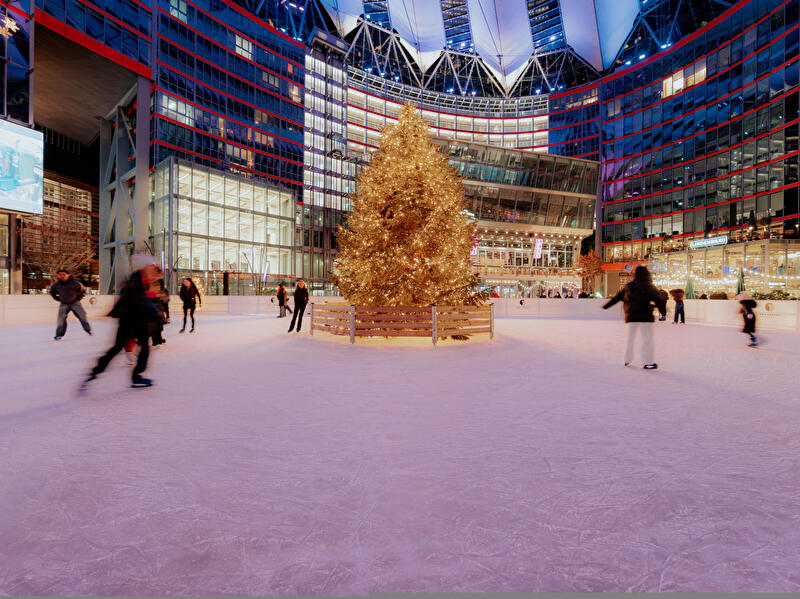Eisbahn mit beleuchtetem Weihnachtsbaum in der Mitte und Menschen beim Schlittschuhlaufen vor dem Sony Center am Potsdamer Platz