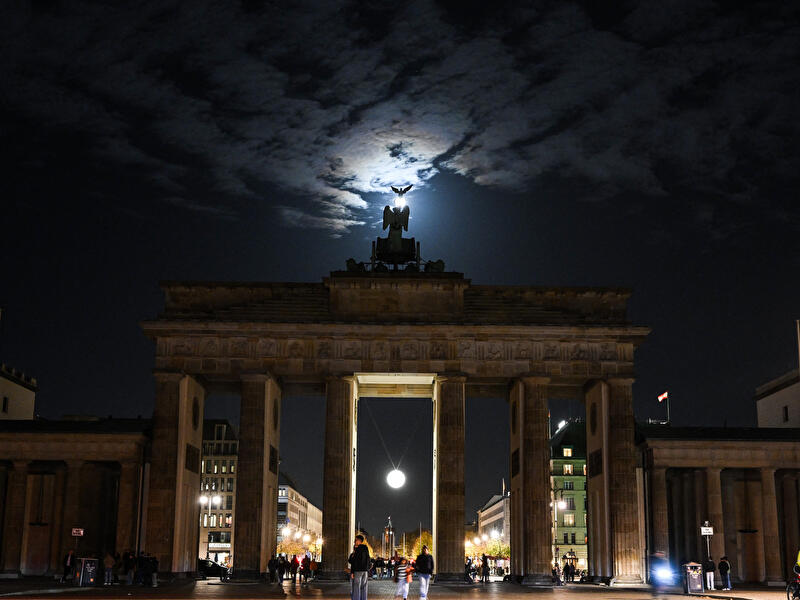 Die Mondleuchte, eine leuchtende Kugel, hängt im mittleren Durchgang des Brandenburger Tors, über dem der Mond am Himmel steht.