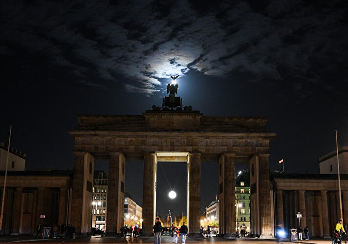 Die Mondleuchte, eine leuchtende Kugel, hängt im mittleren Durchgang des Brandenburger Tors, über dem der Mond am Himmel steht.