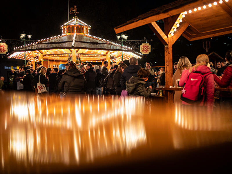 Besucherinnen und Besucher auf einem festlich beleuchteten Weihnachtsmarkt am Abend.