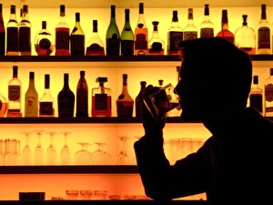 Ein Bar-Besucher sitzt trinkend neben einem Flaschenregal