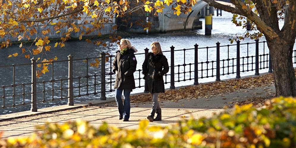 Zwei Frauen spazieren in Berlin bei Sonnenschein im Herbst an der Spree entlang.