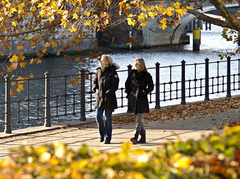 Zwei Frauen spazieren in Berlin bei Sonnenschein im Herbst an der Spree entlang.