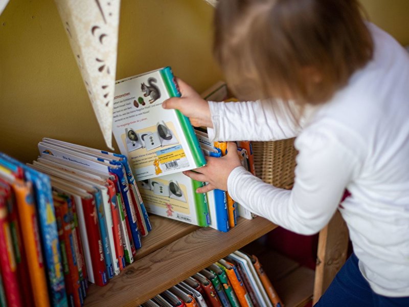 Ein Mädchen nimmt sich ein Kinderbuch aus dem Regal