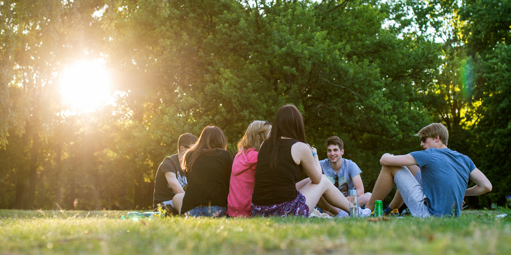 Mehrere Jugendliche sitzen zusammen auf der Wiese in der Sonne.
