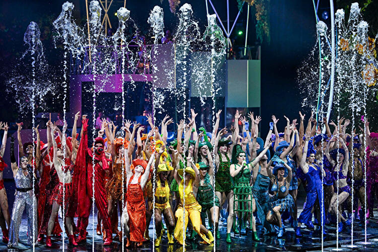 Das Ensemble des Friedrichstadt-Palast steht in farbenfrohen Kostümen, Wasserspielen und choreografierter Tanzszene auf der Bühne.