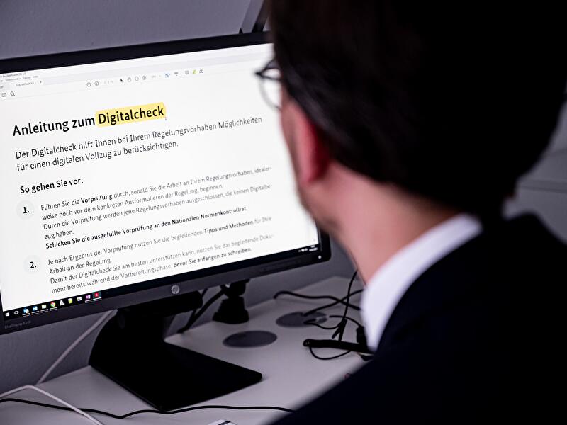 Ein Mann im Anzug sitzt vor einem Computerbildschirm und liest die "Anleitung zum Digitalcheck", ein Online-Dokument mit Erläuterungen zur Vorprüfung von Regelungsvorhaben.