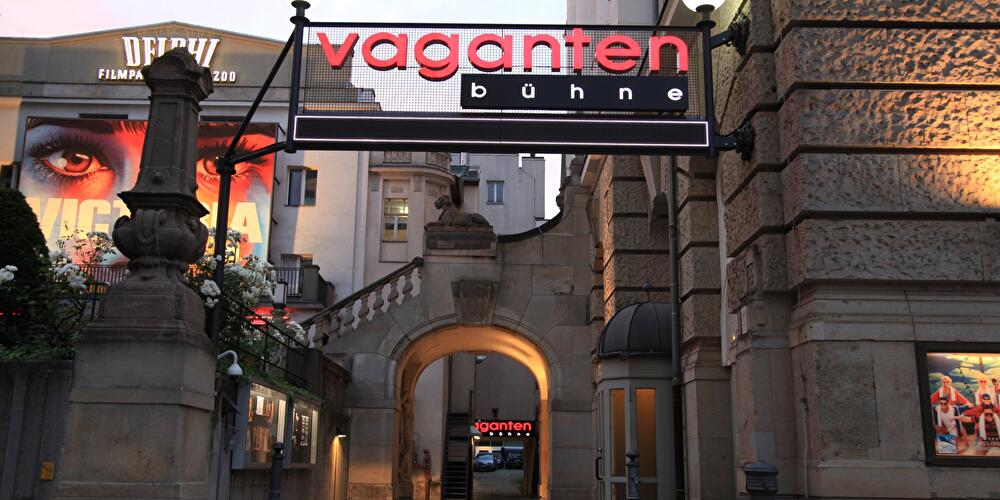 Beleuchteter Schriftzug "Vagantenbühne" über einer Toreinfahrt in der Berliner Kantstraße, im Hintergrund das Delphi-Filmpalast-Kino, in der Abenddämmerung.