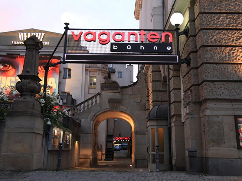 Beleuchteter Schriftzug "Vagantenbühne" über einer Toreinfahrt in der Berliner Kantstraße, im Hintergrund das Delphi-Filmpalast-Kino, in der Abenddämmerung.