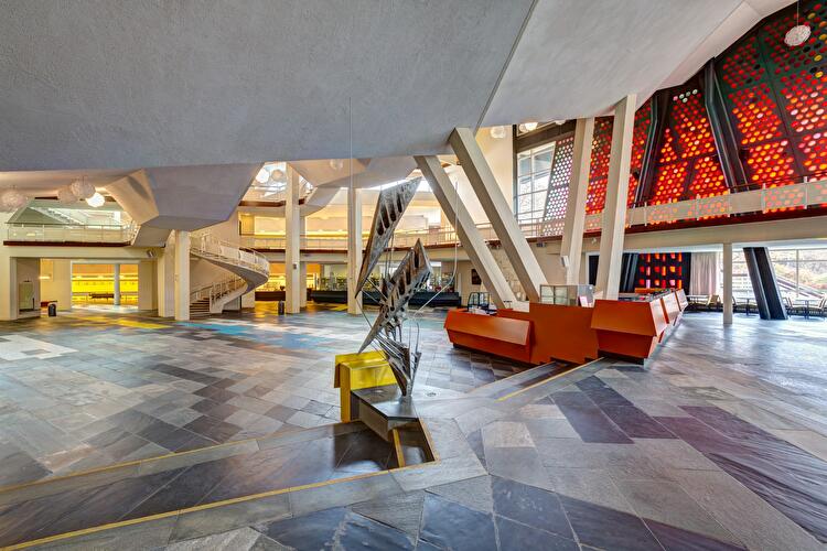 Foyer der Berliner Philharmonie mit roter Empfangstheke, Skulptur, geschwungener Treppe und farbigen Glasflächen.