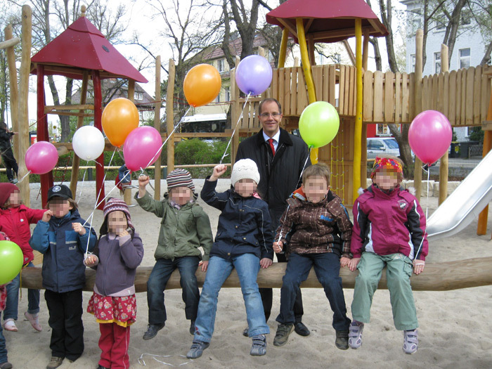 Kinder sitzen auf einem Balken mit Luftballons Spielplatz Wilhelmplatz