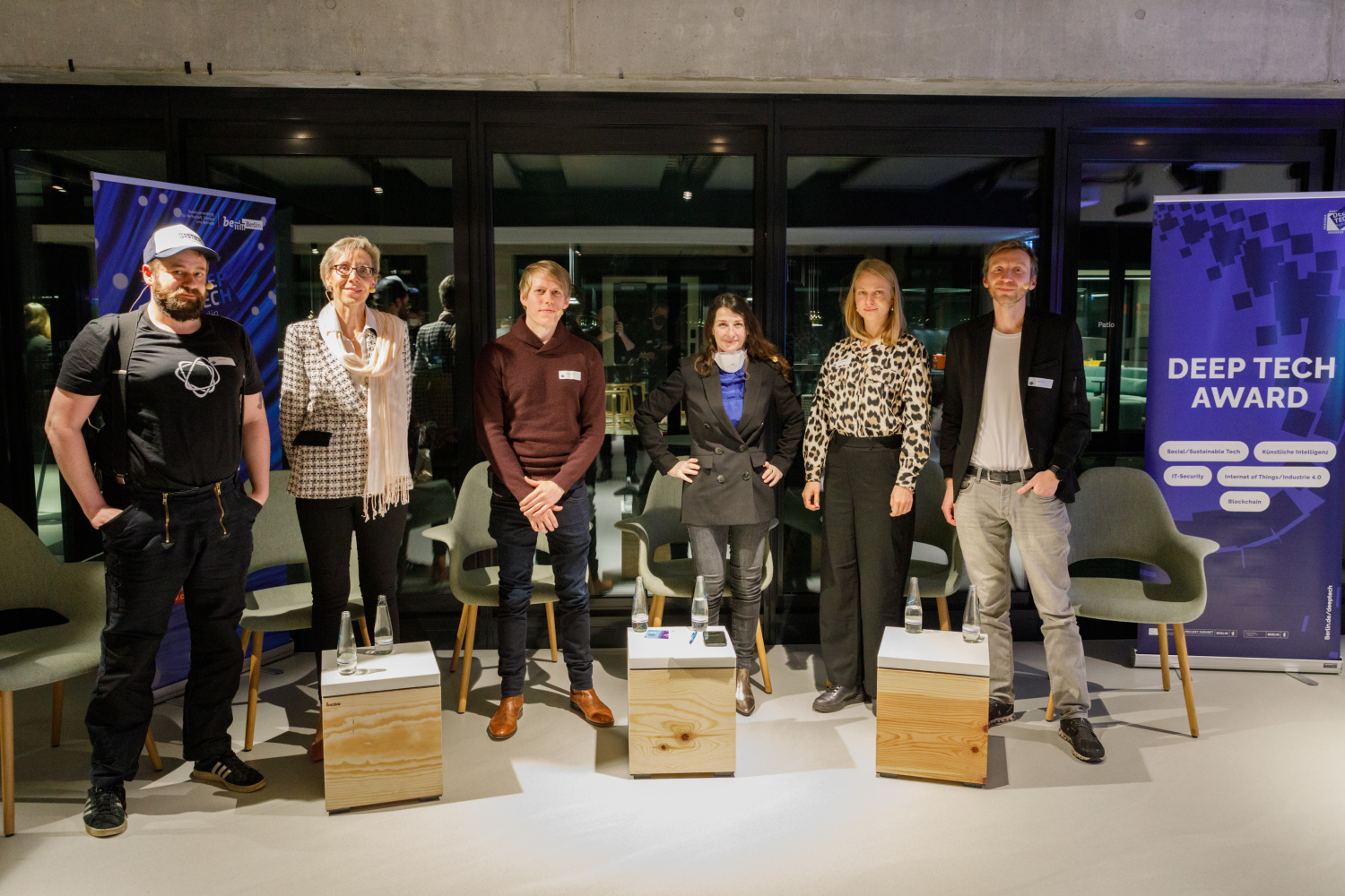 Die Panelist:innen und die Moderatorin stehen vor einer Glaswand