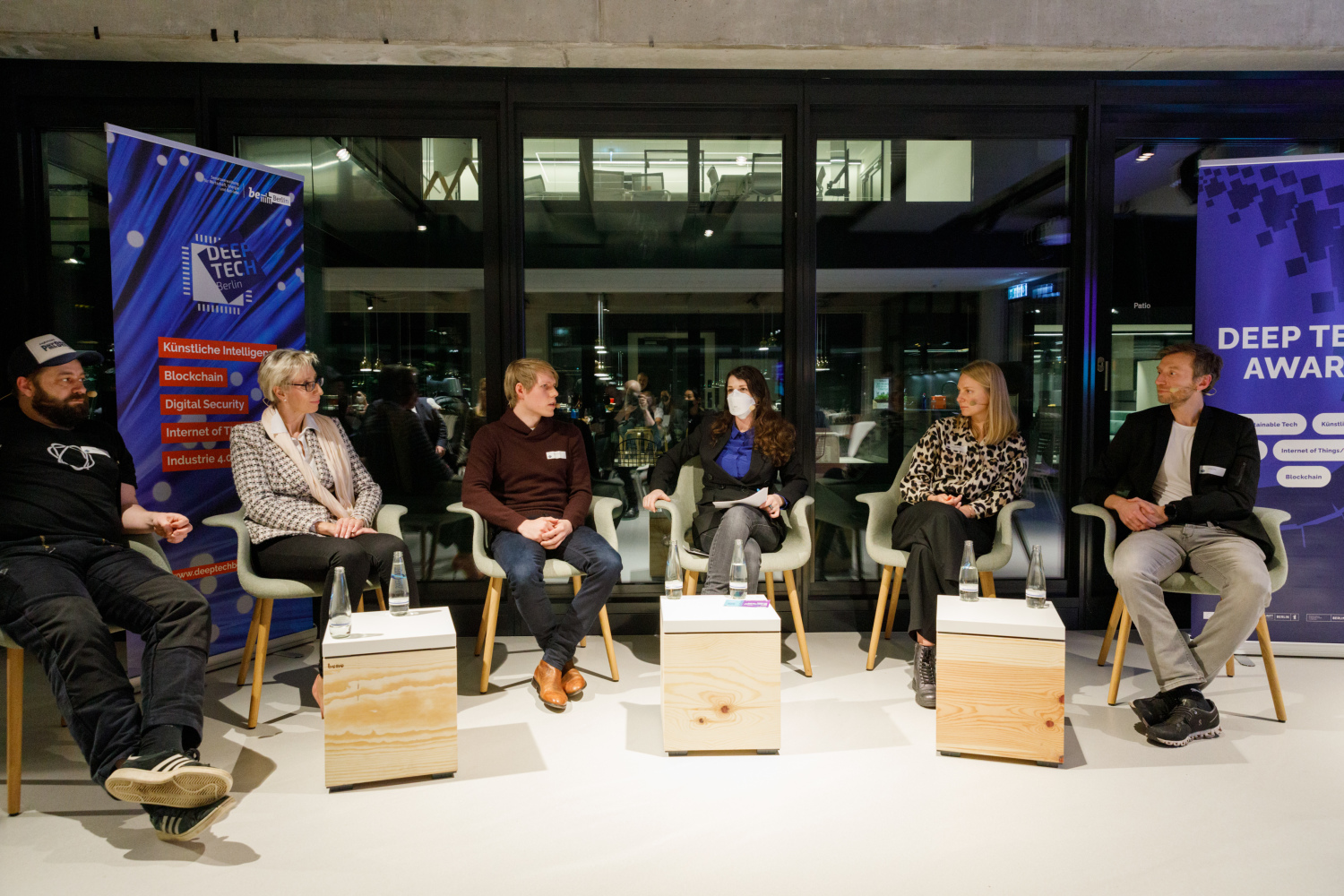 Panelist:innen und Moderatorin auf Stühlen vor Glaswand