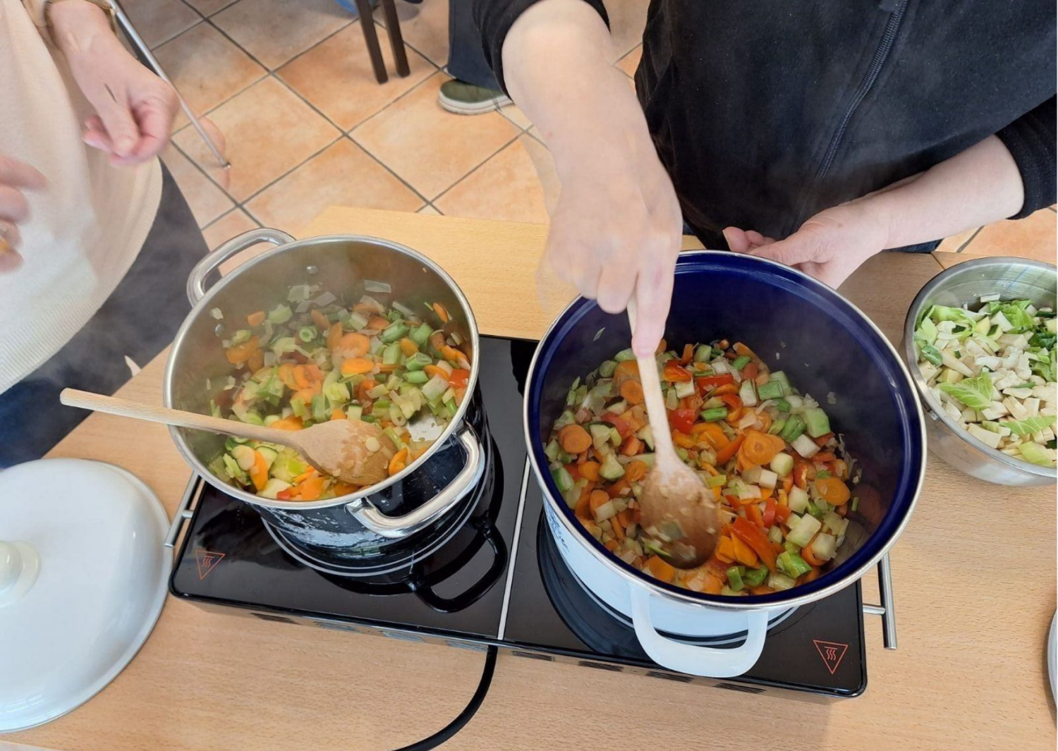 Auf einer Kochplatte wird in zwei Töpfen Gemüsesuppe gekocht