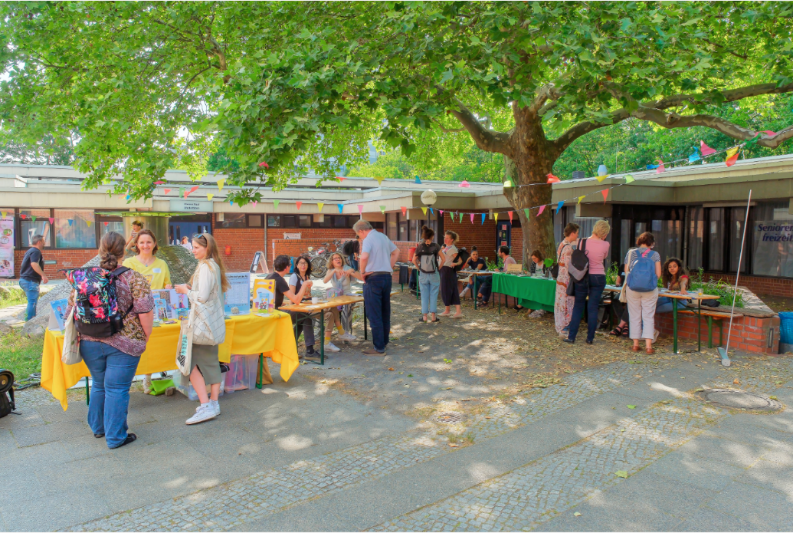 mehrere Menschen besuchen Infostände in einem Innenhof mit einem Baum