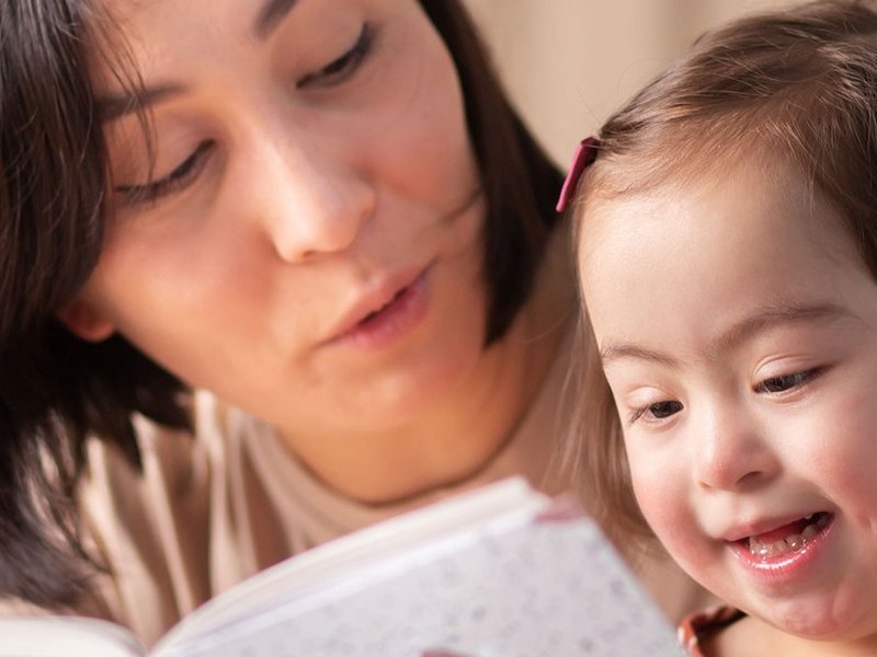 Eine Mutter liest gemeinsam mit ihrer Tochter, die Trisomie 21 hat.