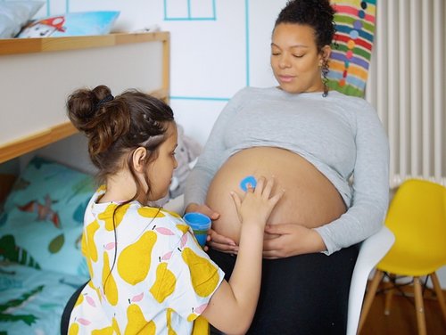 Mädchen malt auf den Bauch der schwangeren Mutter.