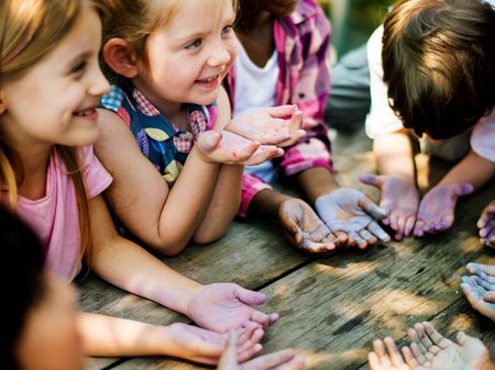 Kitakinder sitzen an einem Holztisch und legen ihre bemalten Hände in einen Kreis.