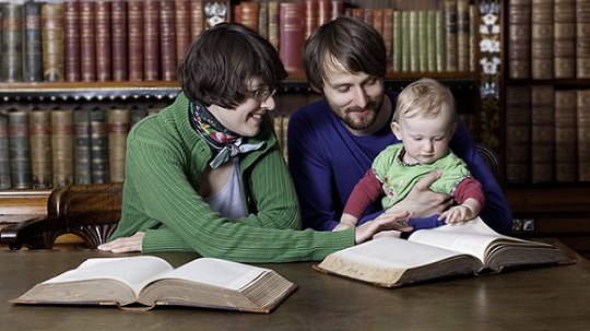 Studierendes Elternpaar mit Baby in einer Bibliothek.