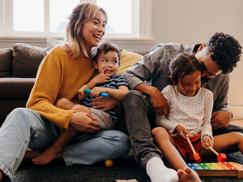 Eine Familie mit zwei Kindern spielt im Wohnzimmer auf dem Boden.