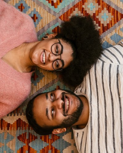 Mann und Frau liegen auf einem Teppich, schauen sich grinsend an