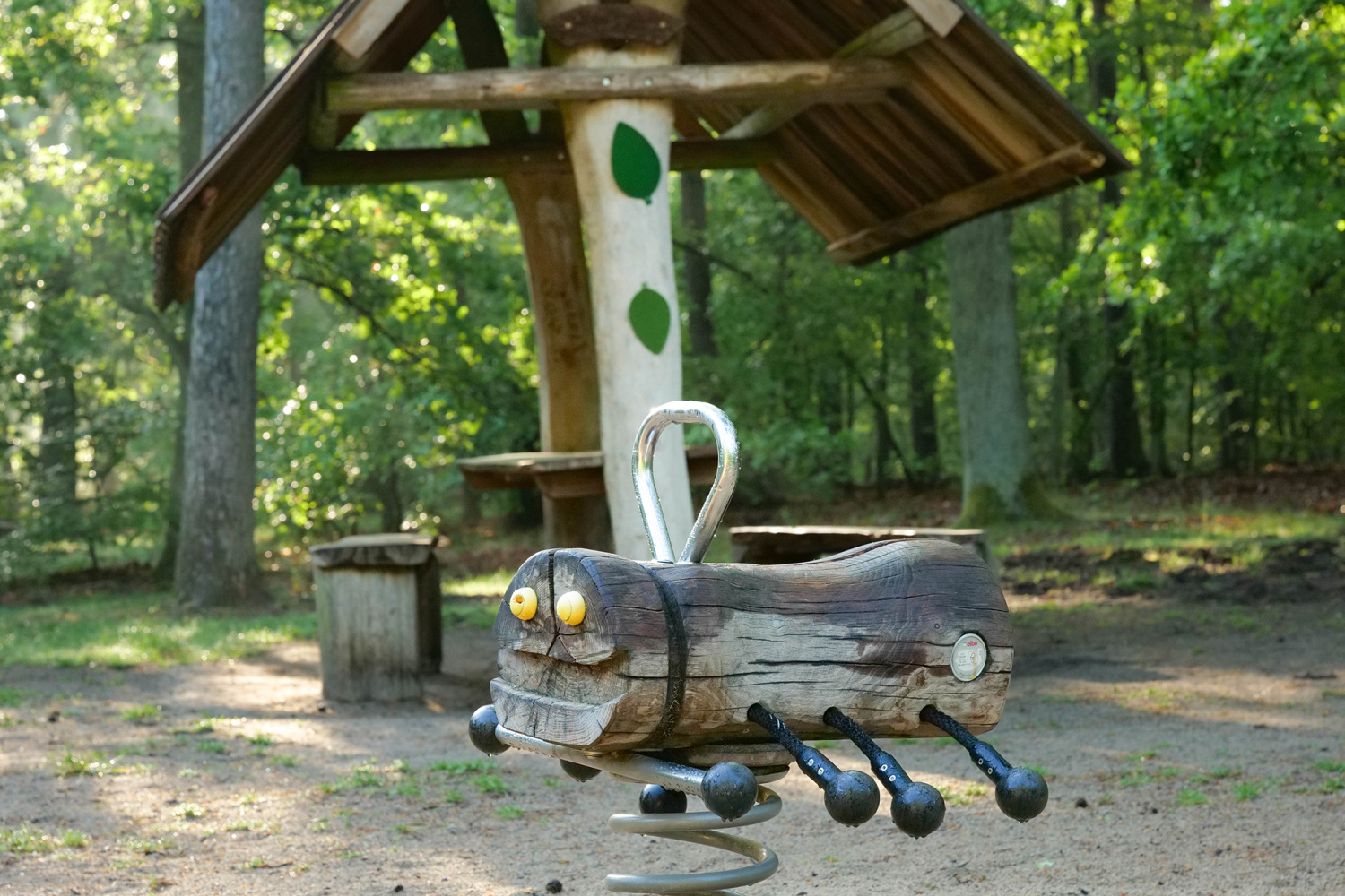 Waldspielplatz Promenade Teufelssee; hölzerne Federwippe, im Hintergrund überdachter Picknickplatz