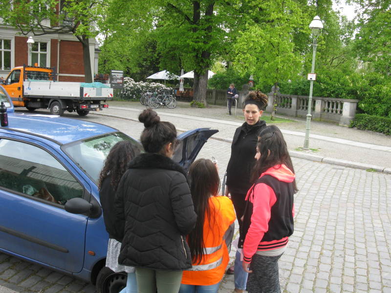 mehrere Maedchen und eine Frau stehen vor einem Auto