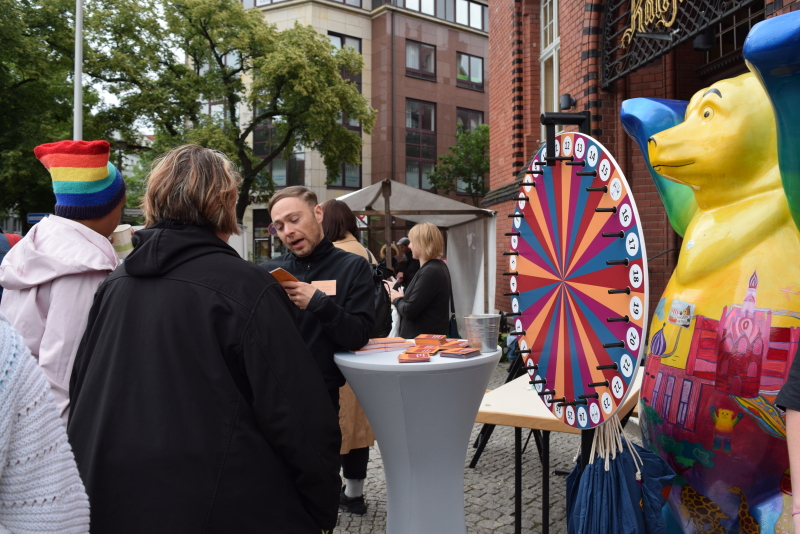 Zwei Frauen beantworten einem Promoter Fragen am Glücksrad, daneben steht ein bunter Berlin-Bär
